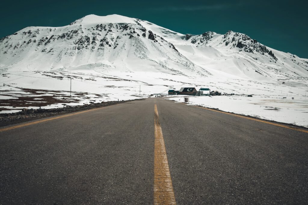 Picturesque winter road leading to snow-covered mountains under a clear sky.