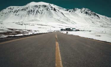 Picturesque winter road leading to snow-covered mountains under a clear sky.
